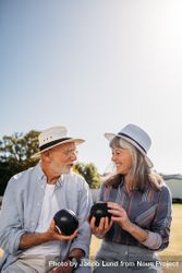 Smiling man and woman sitting together in a park and talking holding boules 0vqOBb