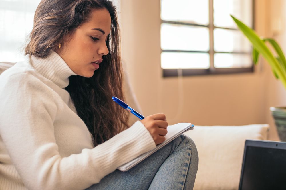 University student studying at home with laptop and notebook