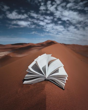 Open book on sand under blue sky