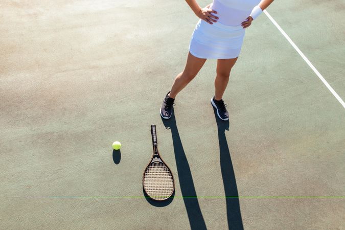 Young woman standing with racket and ball on tennis court