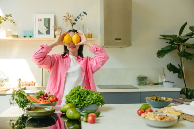 Smiling woman hiding her eyes with two lemons standing in the kitchen