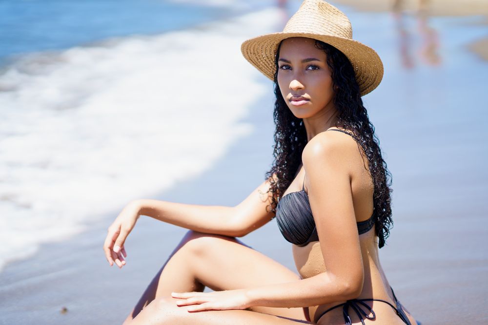 A Young Woman Gracefully Posing with a Straw Hat Amidst Sunlit Waves at the Beach