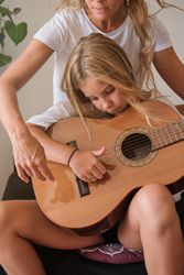 Crop mother and daughter playing guitar together at home