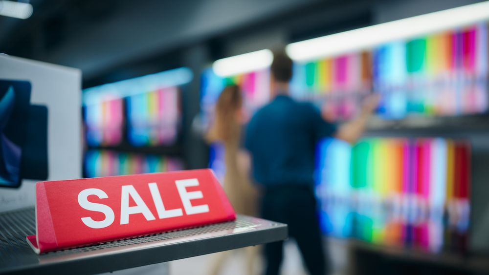 Close Up of a Red Sale Sign in a Home Electronics Department Store with a Range of Modern Smart TV Sets.