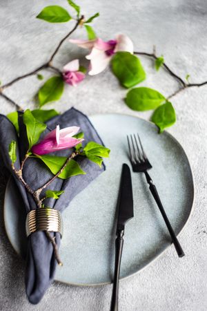 Plate & cutlery with magnolia flowers on grey table