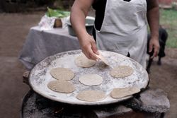 An adult Hispanic woman is cooking traditional corn tortillas over an outdoor stove