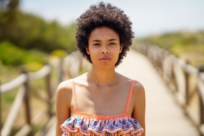 Portrait of woman with afro hair standing on wooden footpath by the coast