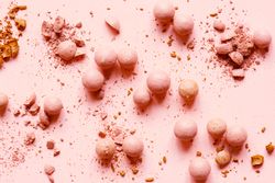 Powdered balls of eyeshadow and blush on pink background