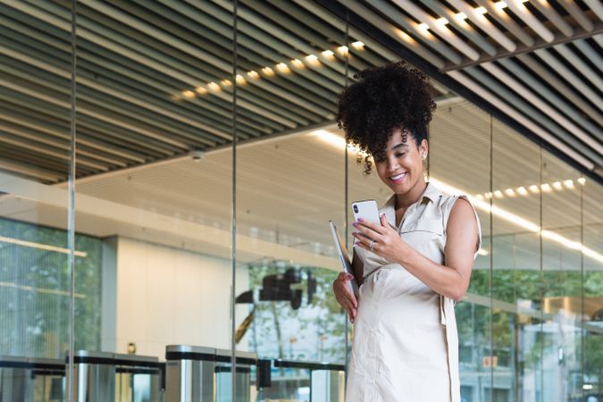Smiling Black pregnant woman using smartphone and carrying laptop