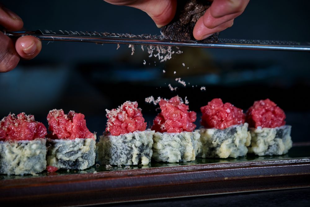 Crop person grating truffle on delicious uramaki sushi rolls with raw tuna