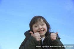 Little girl giving a thumbs up and smiling against a bright blue sky bYgMg5