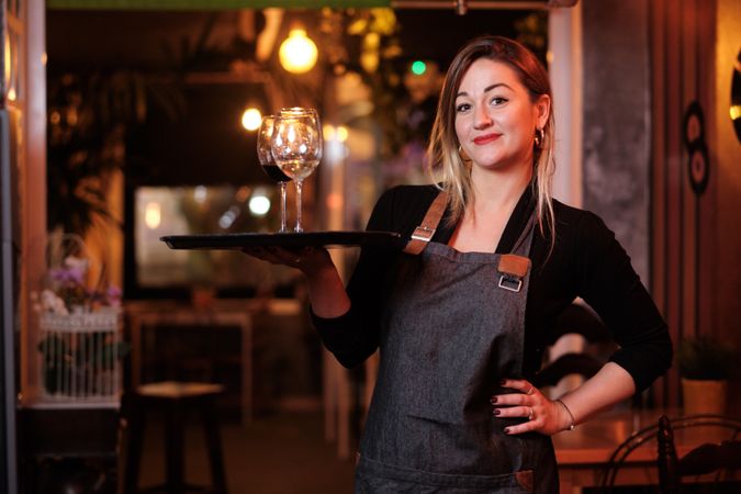Cheerful waitress holding tray with wineglasses