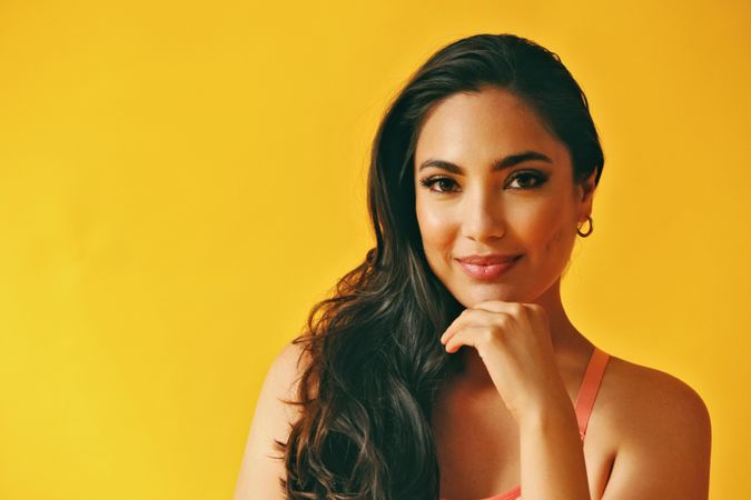 Headshot of calm Hispanic woman looking at camera in yellow room, copy space