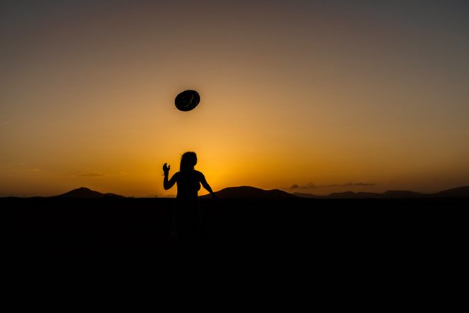 Woman throwing hat into distance to sun