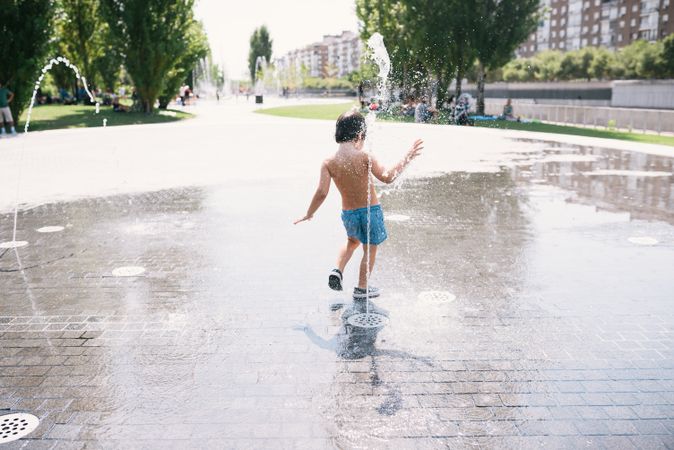 Anonymous kid standing in jet of fountain on street