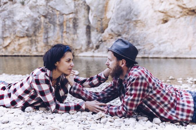 Positive woman and man resting on stone shore near river