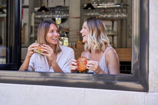 Cheerful female friends eating fast food in cafeteria