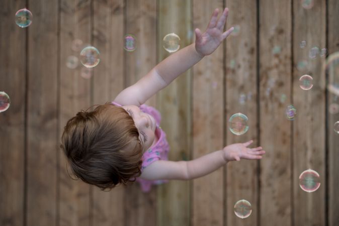 Joyful girl playing with colorful bubbles in wooden ground