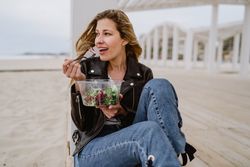 Content woman eating salad from plastic bowl sitting on wooden terrace