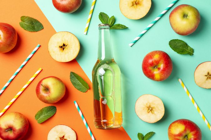 Composition with cider, apples and straws on two tone background
