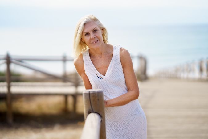 Calm mature female with grey hair leaning on wooden walkway near the coast