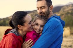 A loving family embracing their daughter who is smiling at the camera.