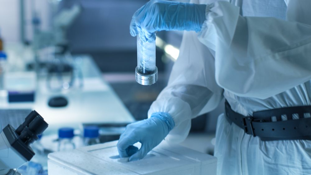 Medical Virology Research Scientist Works in a Hazmat Suit with Mask, Inspects Test Tube with Isolated Virus String from Refrigerator Box.