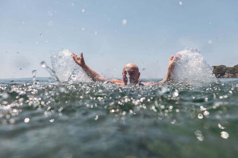 Active mature man swimming and splashing in water