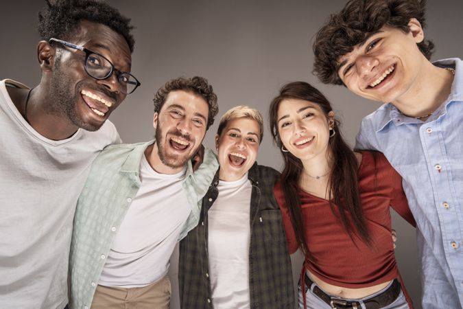 Happy young friends hugging and smiling together in studio portrait on gray background