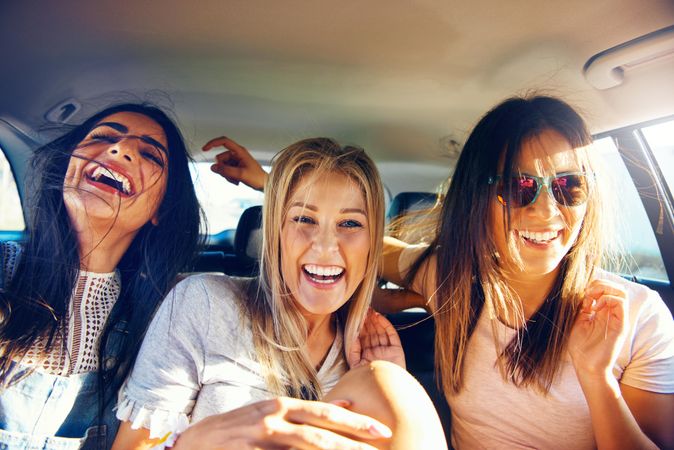 Group of female friends laughing with each other while riding in back of vehicle