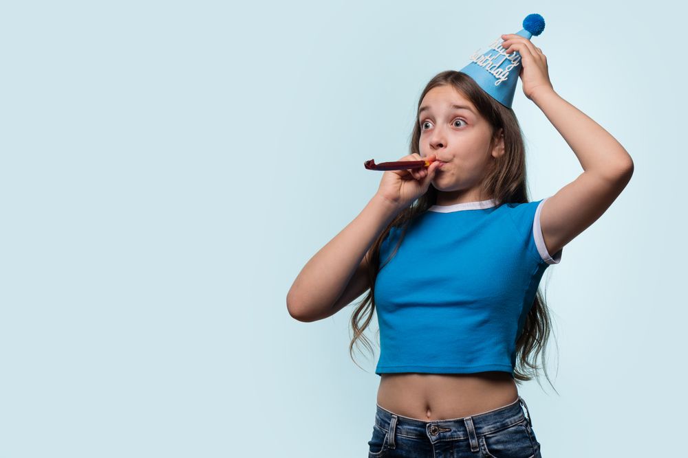 Girl blowing party horn and wearing birthday hat