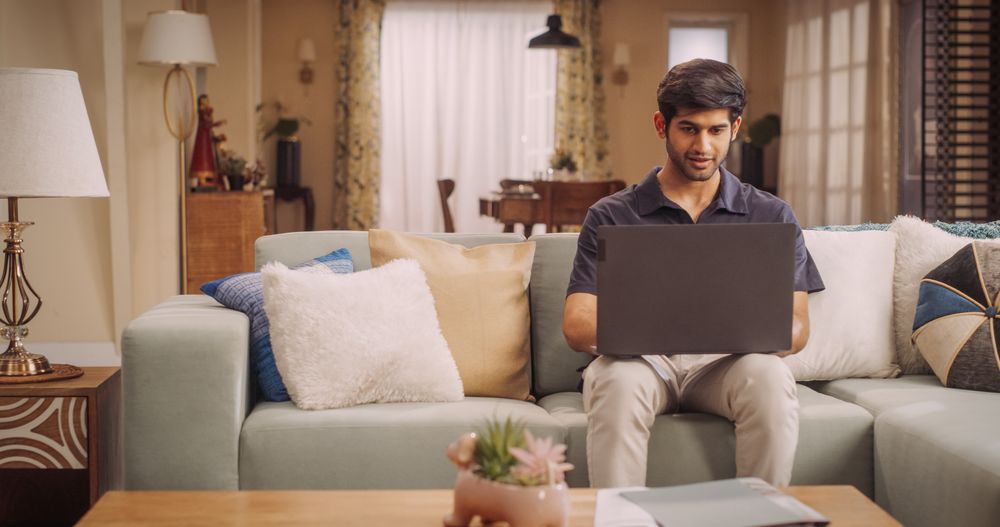 Confident Indian Man, Working Remotely as a Digital Marketer, Using Laptop on Couch at Home.
