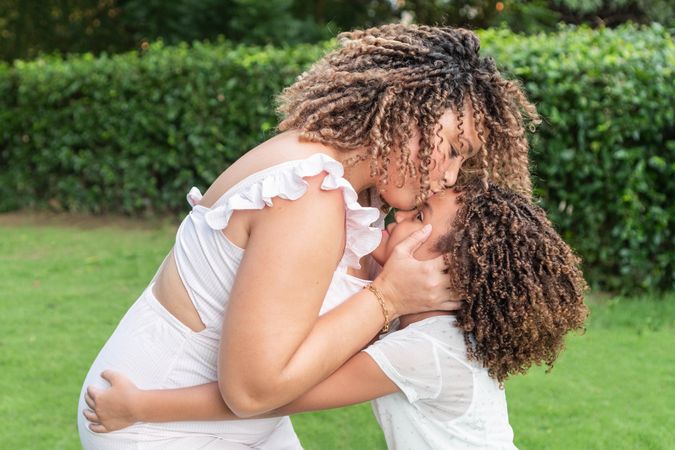 A mother with her eyes closed, kisses her little daughter on the forehead in the open air.
