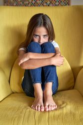 Sad girl sitting in armchair at home