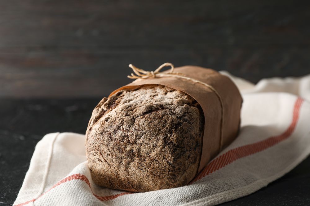 Rye bread on kitchen towel on table against wooden background, space for text and closeup