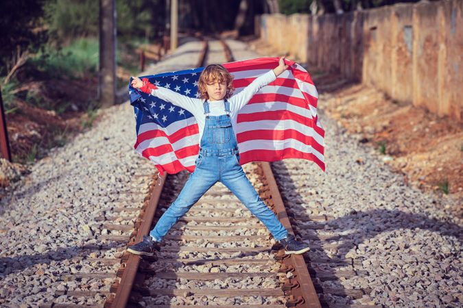 Boy with raised hands and flag of USA on railroad