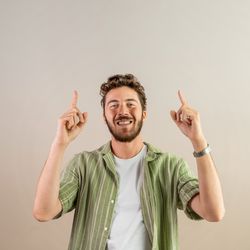 Happy young man pointing up with both fingers on a neutral background.