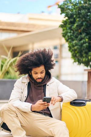 Young man with curly afro hair in the street watching social networks on mobile phone