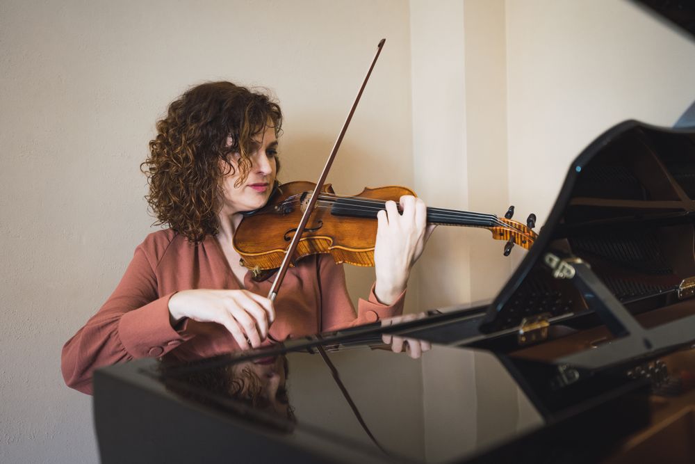 Pregnant woman playing on violin near piano in room