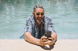 Grey haired man using smartphone in swimming pool