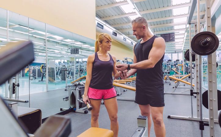 Male trainer working with female client in gym