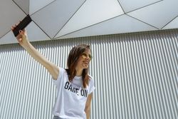Cheerful woman taking selfie and posing near modern wall