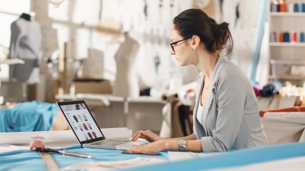 Woman fashion, designer,  Sitting at Her Desk Looking at Sketches on a Laptop, Taking Notes.