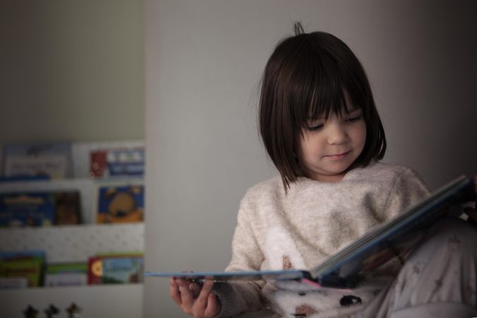 Girl in pajamas reading story in her room
