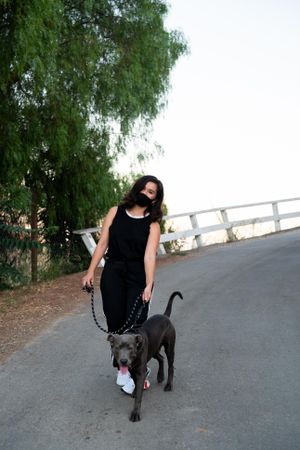 Full length shot of woman with mask walking her dog in the evening smiling and looking at camera