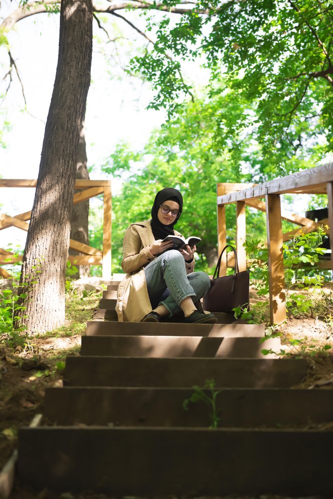 Woman in headscarf calmly reading on the stairs