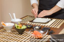 Hands of woman chef preparing sushi rolls with rice on a nori seaweed sheet 5o79G5