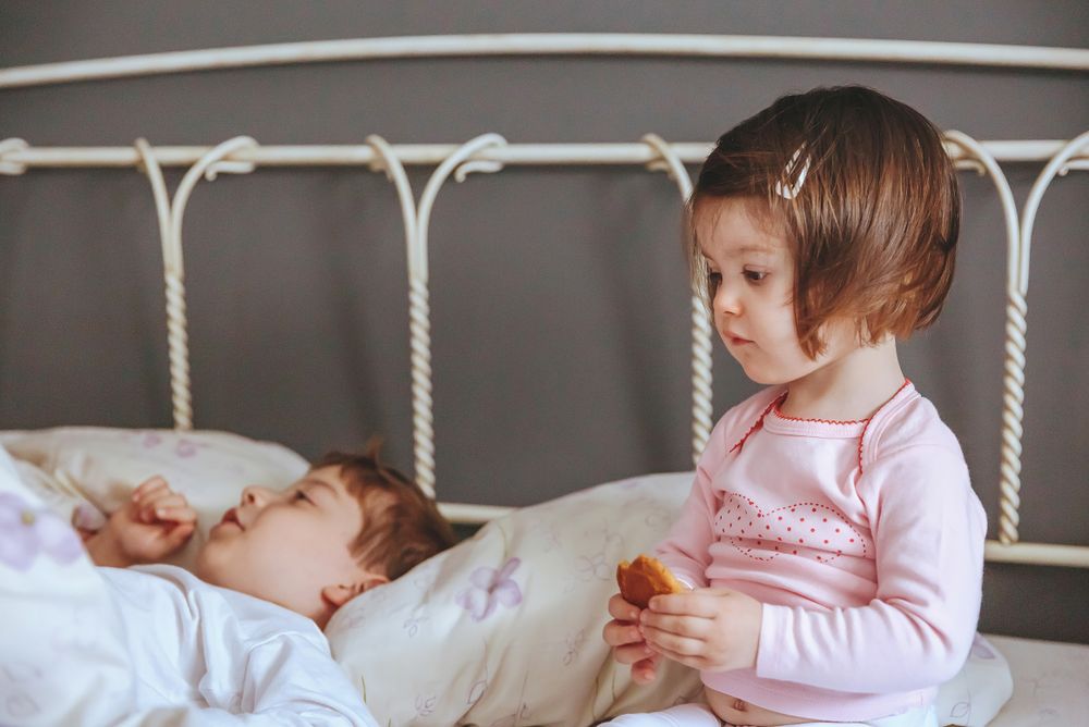 Closeup of thoughtful little girl holding cookie sitting in bed with brother on a relaxed morning