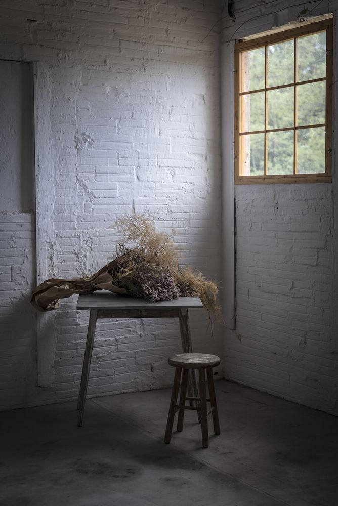 Bunch of plant in paper on table near stool in grey room