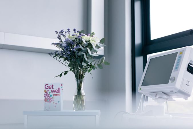 Get well soon wishing card with flower vase on side table in hospital room